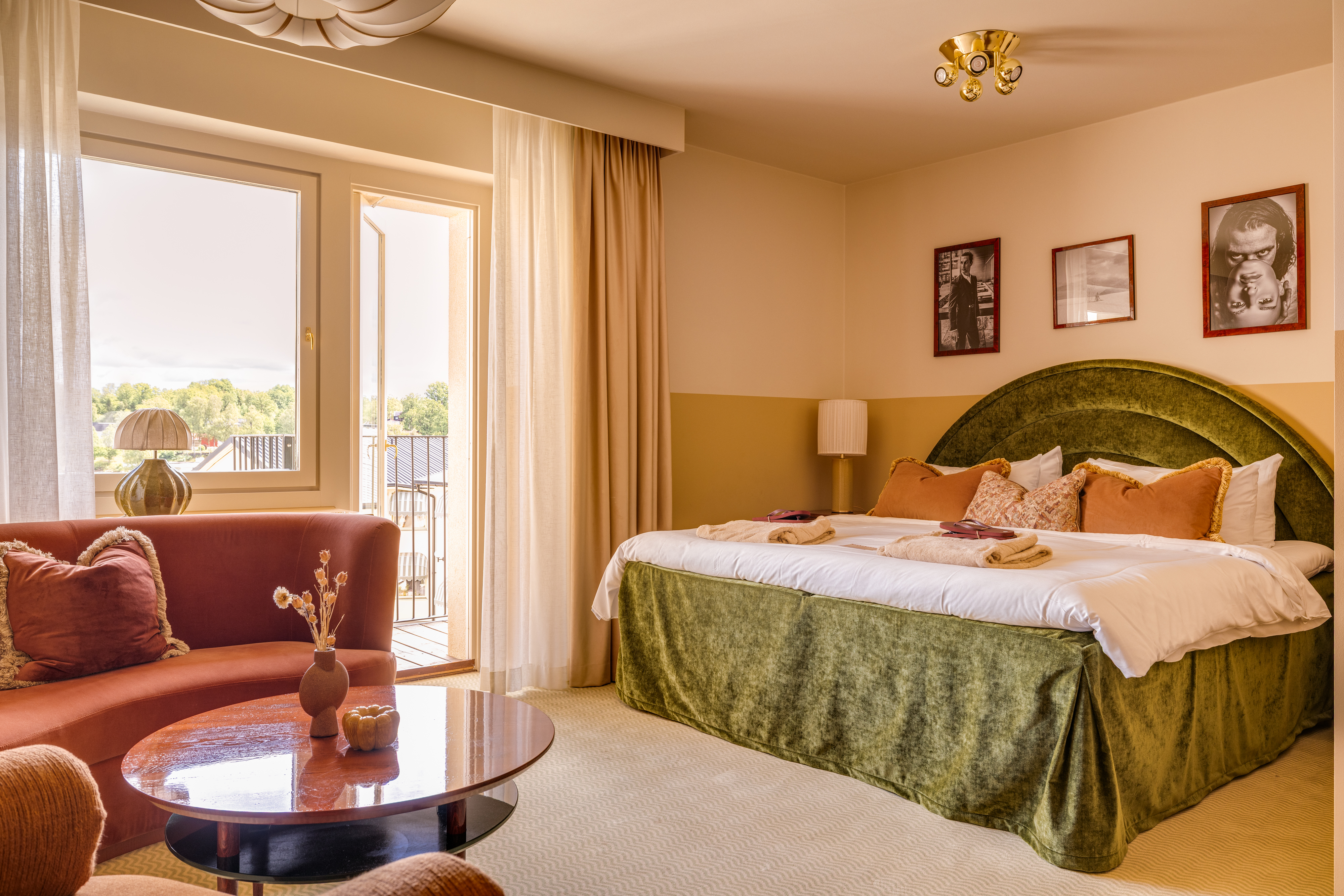Hotellrum med dubbelsäng, grön sänggavel, soffa, soffbord och balkongdörr