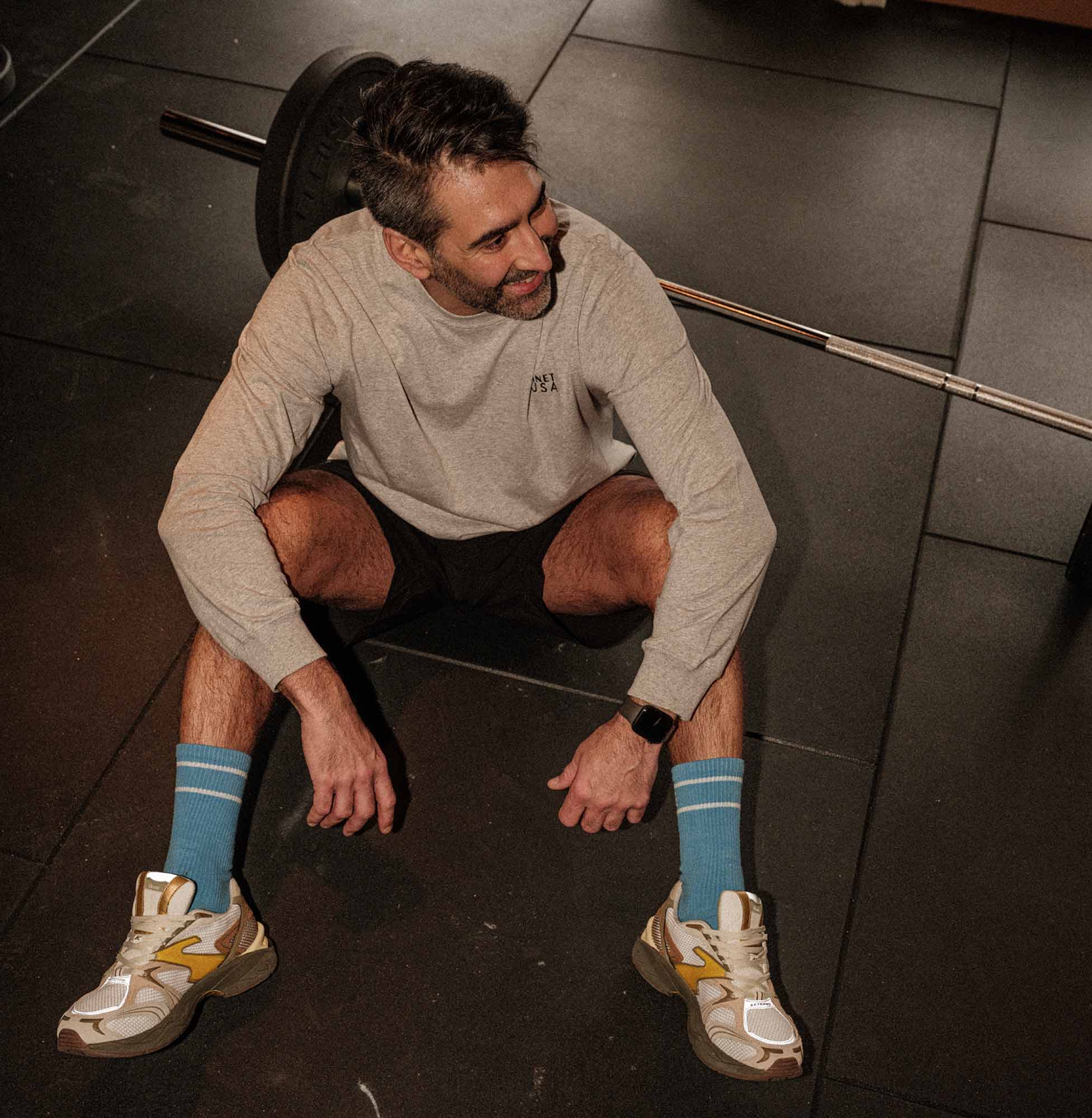 Man sitter på gymgolvet bredvid en skivstång och ler