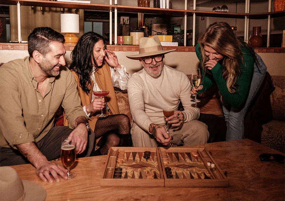 Fyra vänner skrattar och spelar backgammon med öl och vin i lobbybaren på Hjortviken
